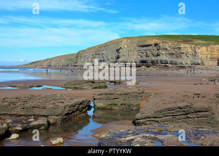 Looking North across the sand and rocky beach of Dunraven bay towards the huge rock cliffs towards Ogmore by sea on a sunny day. Stock Photo
