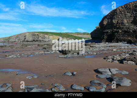 Looking North across the sand and rocky beach of Dunraven bay towards the huge rock cliffs towards Ogmore by sea on a sunny day. Stock Photo