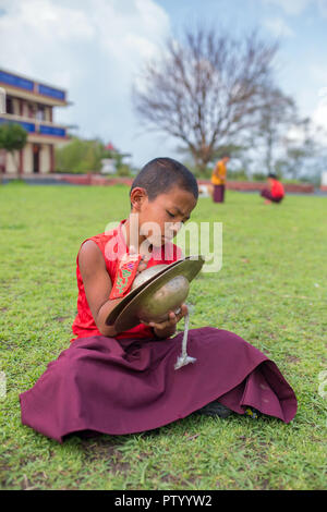 Gangtok, India - May 3, 2017: Unidentified young novice buddhist monk in traditional red robes practicing in playing Tibetan music instrument tingsha  Stock Photo