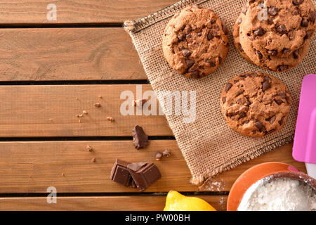 Homemade biscuits with chocolate chips on wooden slatted table with ingredients in a rustic kitchen. Horizontal composition. Top view Stock Photo