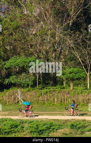 Vang Vieng, Laos - January 19, 2017: Unidentified girls cycling on a rural road in Vang Vieng village, Laos. Stock Photo