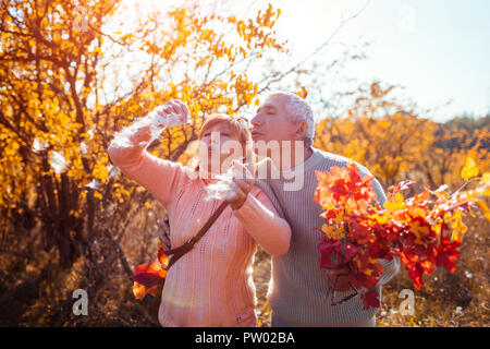 Senior couple walking in autumn forest. Middle-aged man and woman blowing fluffy seeds. People having fun outdoors Stock Photo