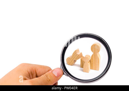 Magnifying glass is looking at a broken wooden figure of a man with a partner and a child. Strife in the family. One parent is broken, addicted to dru Stock Photo