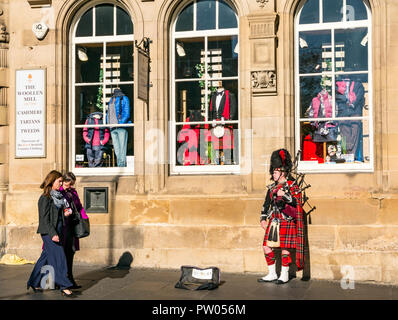 Women walking past street busker in Scottish military uniform with kilt, bearskin hat playing bagpipes, Royal Mile, Edinburgh, Scotland, UK Stock Photo