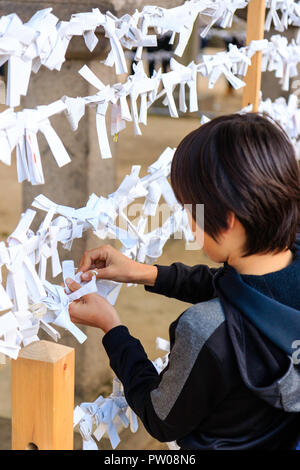 Japanese new year, shogatsu. Young boy, 9-10 years old, tying bad fortune paper slip, Omikuji to frame work to leave bad luck behind. Nishinomiya shri Stock Photo