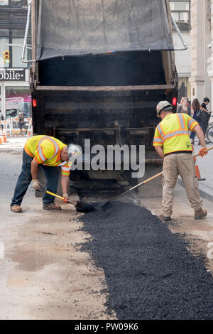 Two construction workers repave a road that had been opened to repair steam pipes, On Waverly Place in Greenwich Village, New York City. Stock Photo