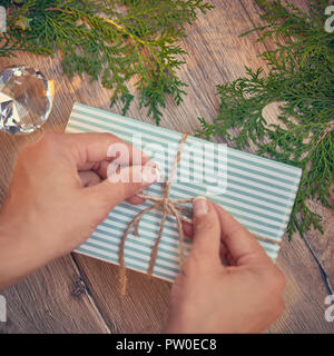 Christmas gift in hands, pine cones, thuja branches on wooden background. Flat lay, top view, copy space. Stock Photo