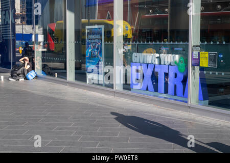 Homeless man sitting outside a halifax bank with a 'Giving you extra'  sign in the window. There is a shadow of another man walking past. London, UK Stock Photo