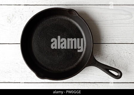 Empty black cast iron pan isolated on white painted wood from above. Stock Photo