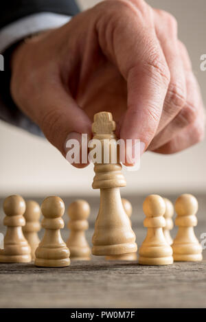 Businessman playing chess moving the king piece lifting it up in his fingers in a close up view with pawns visible behind on the desk for concept abou Stock Photo