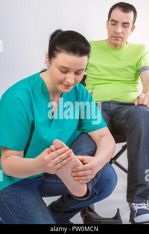 Female physiotherapist massaging foot of young man in wheelchair. People, healthy and care concept. Stock Photo