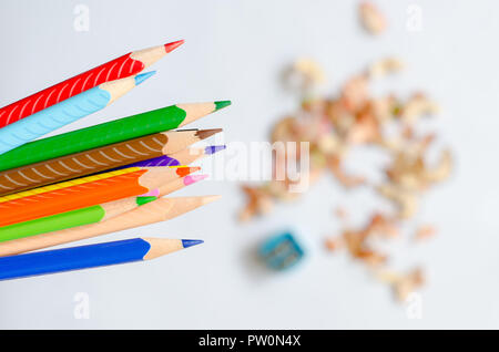 Colored pencils against blurred shavings on white background. Stock Photo