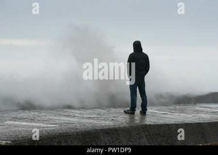 Lyme Regis, Dorset, UK.  12th October 2018. UK Weather.   A man watches the huge waves from Storm Callum crash against the historic Cobb harbour at Lyme Regis in Dorset.  Picture Credit: Graham Hunt/Alamy Live News Stock Photo