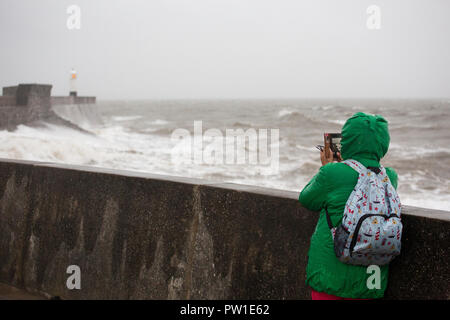 Porthcawl, Wales, UK. Friday 12 October 2018.  A young woman takes a picture as Storm Callum batters the lighthouse at Porthcawl in south Wales Credit: Gruffydd Thomas/Alamy Live News Stock Photo