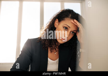 Stressed out businesswoman sitting at her desk holding her forehead looking at computer. businesswoman with curly hair in formal clothes looking at co Stock Photo