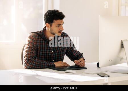 Man sitting at his desk in office writing on a digital writing pad looking at the computer. Entrepreneur making notes using electronic writing pad sit Stock Photo