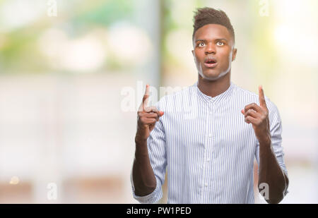 Young african american man over isolated background amazed and surprised looking up and pointing with fingers and raised arms. Stock Photo