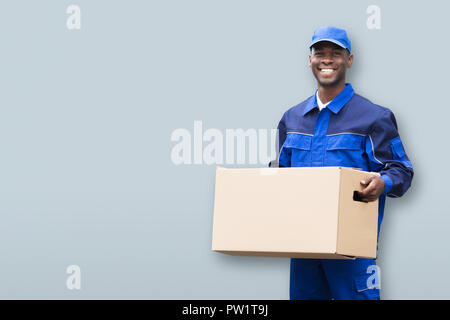 Smiling Male African Mover Holding Package On Gray Background Stock Photo