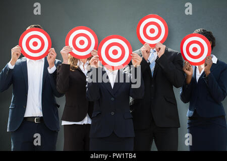 Group Of Businesspeople Hiding Their Faces Behind Dartboard On Grey Background Stock Photo