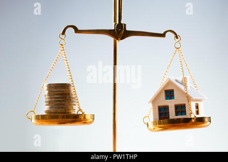 Close-up Of Stacked Coins And House Model Balancing On Golden Justice Scale Stock Photo