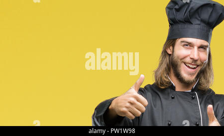 Young handsome cook man with long hair over isolated background approving doing positive gesture with hand, thumbs up smiling and happy for success. L Stock Photo