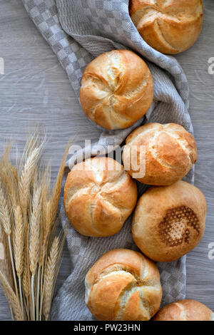 Crusty round bread rolls, known as Kaiser or Vienna rolls scattered on linen towel on light wood, flat lay Stock Photo