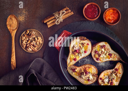 Pears baked with Blue cheese and walnuts, served with orange and cowberry jam, cinnamon and sugar on dark background. Top view Stock Photo