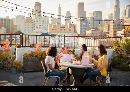 Female Friends Celebrating Birthday On Rooftop Terrace With City Skyline In Background Stock Photo