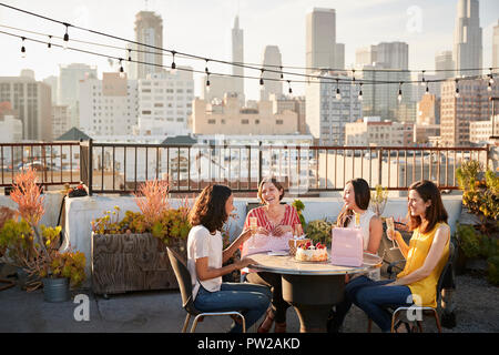 Female Friends Celebrating Birthday On Rooftop Terrace With City Skyline In Background Stock Photo