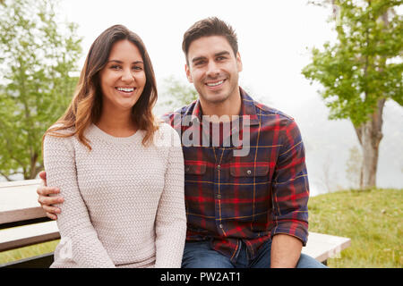 Young smiling couple sit embracing in a park Stock Photo