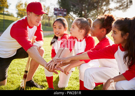 Girl baseball team kneeling with their coach, touching hands Stock Photo