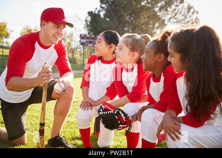 Girl baseball team kneeling in a huddle with their coach Stock Photo
