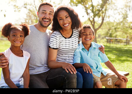 Outdoor Portrait Of Smiling Family Sitting On Bench In Park Stock Photo