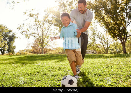 Father And Son Playing Soccer In Park Together Stock Photo