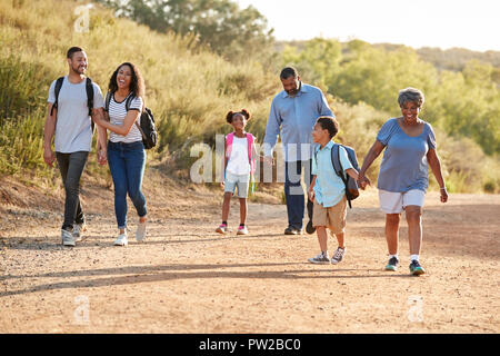 Multi Generation Family Wearing Backpacks Hiking In Countryside Together Stock Photo