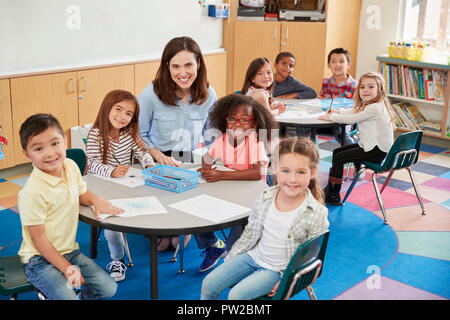 Female school teacher and kids in class smiling to camera Stock Photo