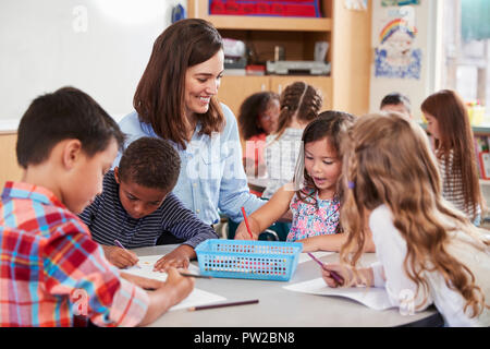 Teacher sitting at table with young school kids in lesson Stock Photo