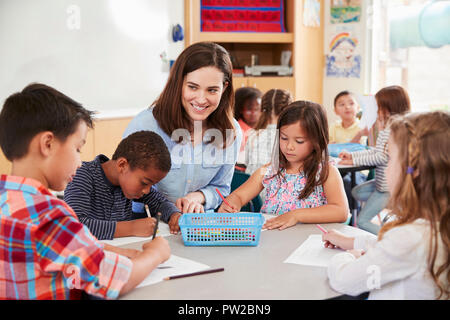 Teacher sitting at table with young school kids in classroom Stock Photo