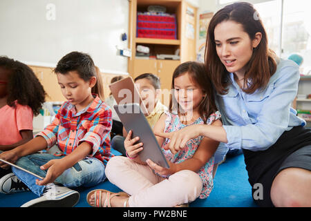 Teacher helps girl in elementary class with tablet computers Stock Photo