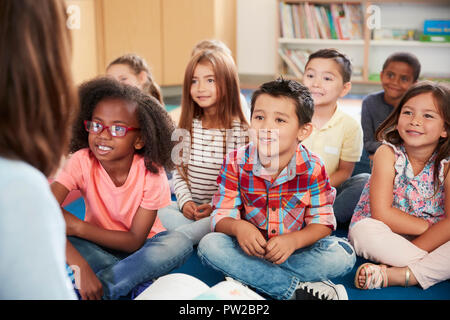 Elementary school kids sit on floor looking up at teacher Stock Photo