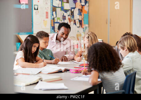 Male teacher works with elementary school kids at their desk Stock Photo