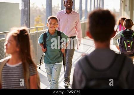 Male teacher and pupils walking on busy school campus Stock Photo