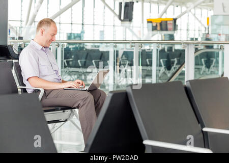 Man working on his laptop while waiting for an airplane in the airport Stock Photo