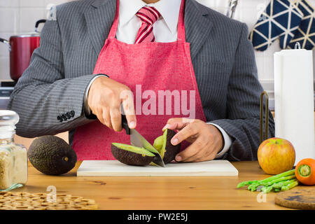 A businessman, father, husband and red tie wearing apron and holding a small peeled banana in the kitchen. Stock Photo