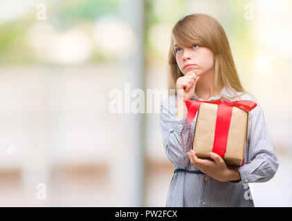 Young blonde toddler holding a present serious face thinking about question, very confused idea Stock Photo