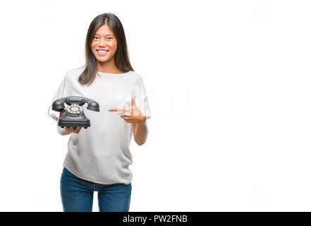 Young asian woman holding vintagera telephone over isolated background very happy pointing with hand and finger Stock Photo