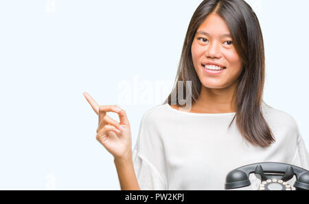 Young asian woman holding vintagera telephone over isolated background very happy pointing with hand and finger to the side Stock Photo