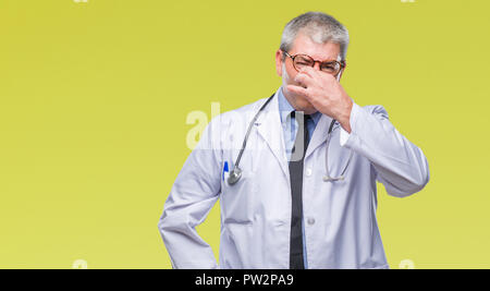 Handsome senior doctor man over isolated background smelling something stinky and disgusting, intolerable smell, holding breath with fingers on nose.  Stock Photo