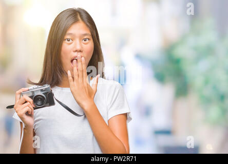 Young asian woman holding vintagera photo camera over isolated background cover mouth with hand shocked with shame for mistake, expression of fear, sc Stock Photo