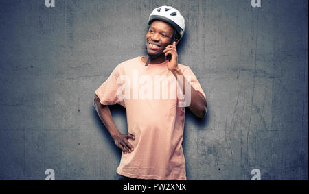 Black man wearing bike helmet happy talking using a smartphone mobile phone Stock Photo